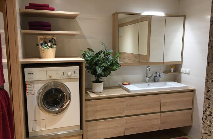 Ein Badezimmer in Holzdekor mit großzügigem Waschtisch, Spiegelschrank und Waschmaschinenverbau